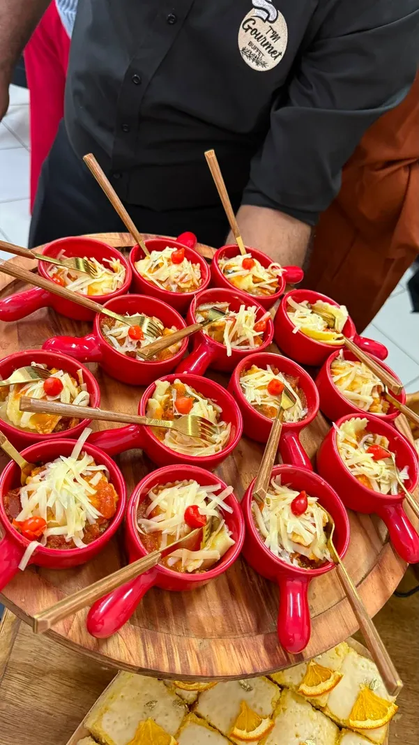Garçom do buffet servindo mini caçarolas de massa recheada com queijo e pimenta biquinho em travessa de madeira