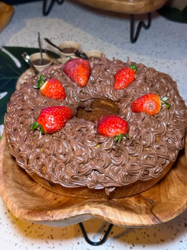 Bolo artesanal com cobertura cremosa de brigadeiro e morangos frescos servido em suporte de madeira