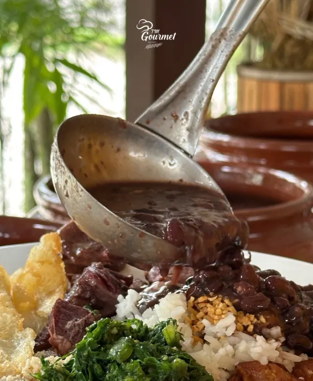 Feijoada sendo servida no prato com arroz, farofa e couve