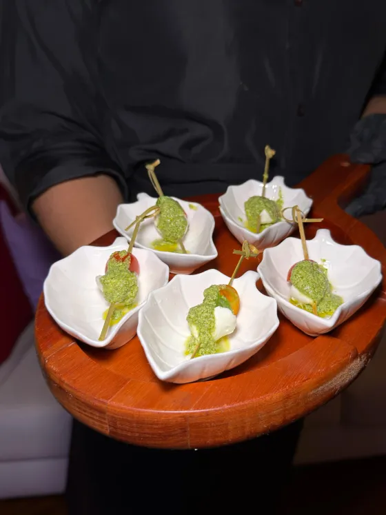 Garçom servindo canapés de muçarela de búfala com pesto em cumbucas individuais