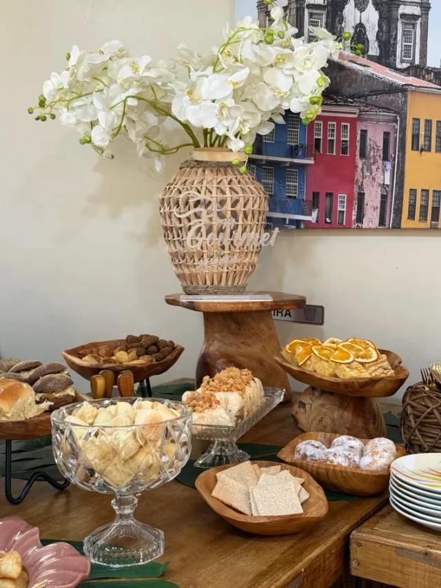 Mesa de boas-vindas e coffee break com mini sanduíches artesanais, pães, bolos com laranja e arranjo floral TM Gourmet