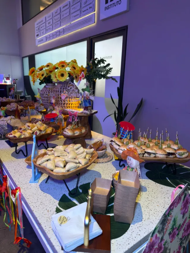 Mesa de buffet temático para eventos com mini pastéis assados, mini sanduíches e arranjos florais