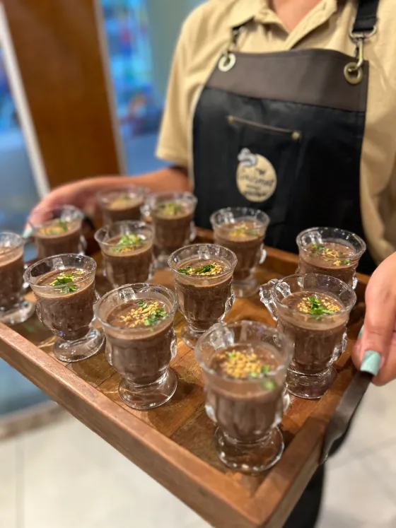 Garçonete servindo caldinhos de feijão em copinhos de vidro